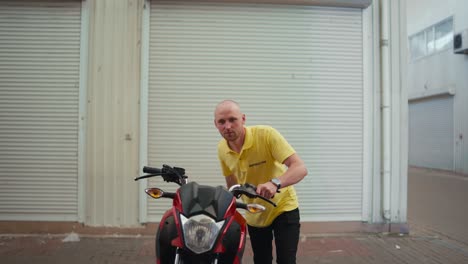 A-bald-man-driving-instructor-in-a-yellow-T-shirt-drives-a-red-moped-into-the-garage