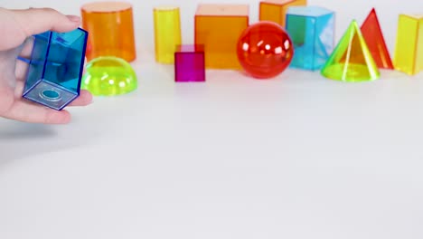 a hand interacts with colorful 3d geometric shapes on a white table, highlighting various forms and colors