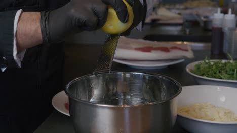 a chef skillfully zests a lemon, the fresh zest falling directly into a bowl below