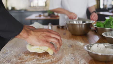 Mixed-race-male-chef-kneading-dough-on-a-kitchen-table