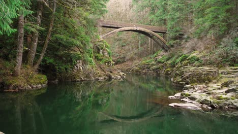 Water-reflects-wooden-arch-bridge-spanning-Lewis-River,-static-shot