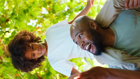 Vertical-Video-Of-Father-And-Son-In-Summer-Garden-With-Boy-Riding-On-Dads-Shoulders