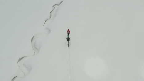 two people skiing through snowy mountain terrain in kyrgyzstan, aerial view