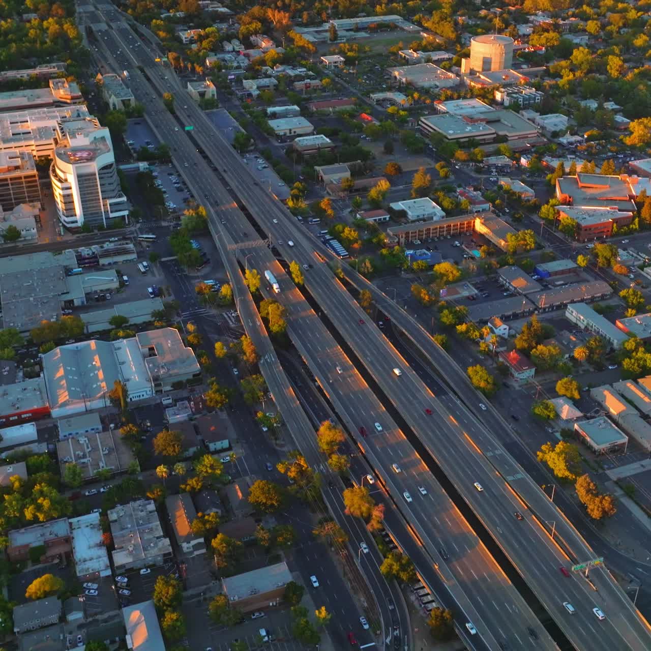 Multilane two-ways roads along the big city. Green city panorama in the rays of setting sun. Aerial view