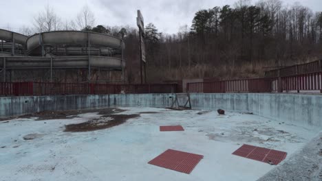 slider footage of an empty pool in an abandoned rural water park with unused waterslides in the background