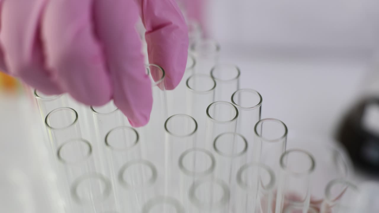 Close-up of a hand in a pink glove handling test tubes in a laboratory