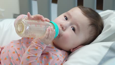 pequeña niña caucásica bebiendo las últimas gotas de leche de fórmula sosteniendo el biberón con las dos manos