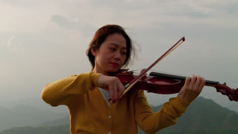 camera orbiting around a close-up of a woman playing the violin on a mountainside