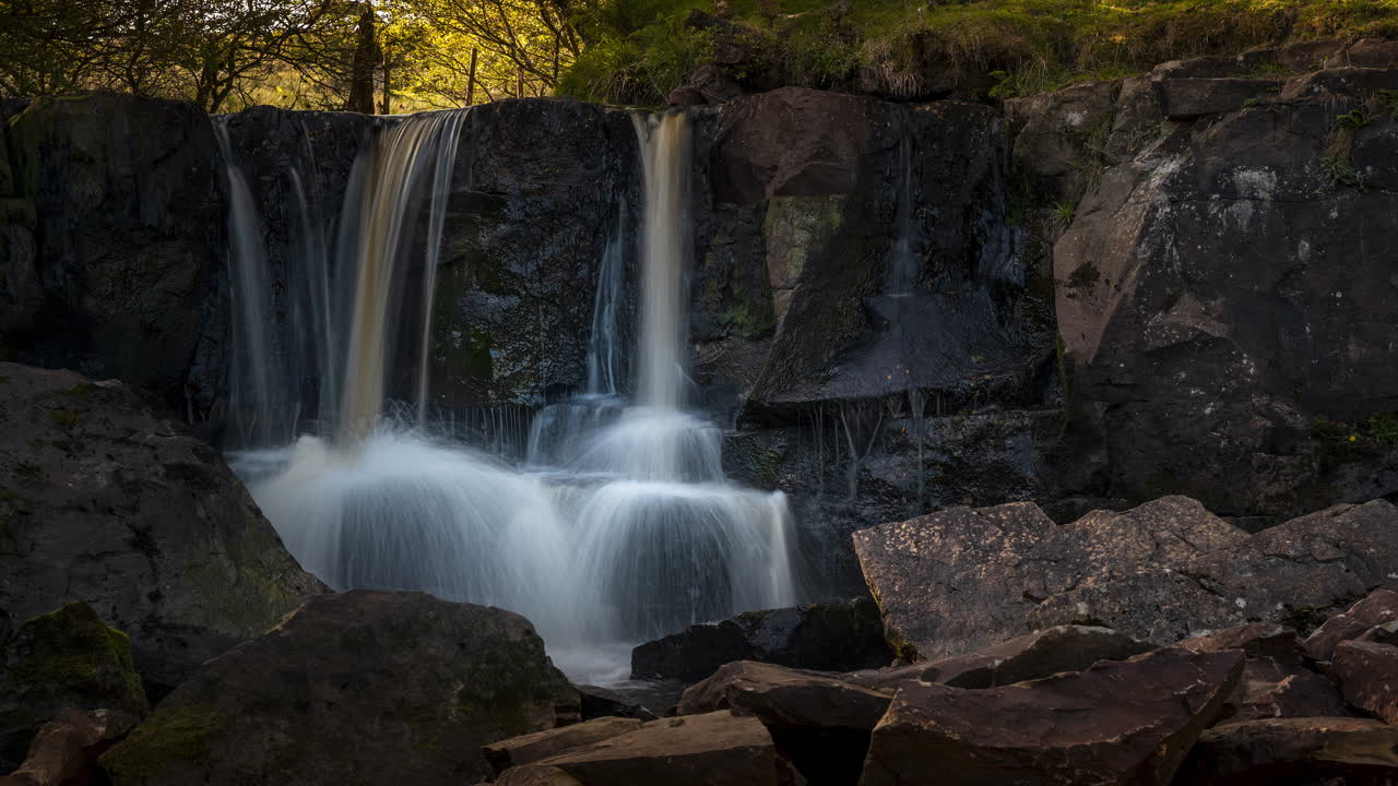 Zeitraffer eines lokalen Wasserfalls in einer ländlichen Waldlandschaft Irlands an einem sonnigen Sommertag