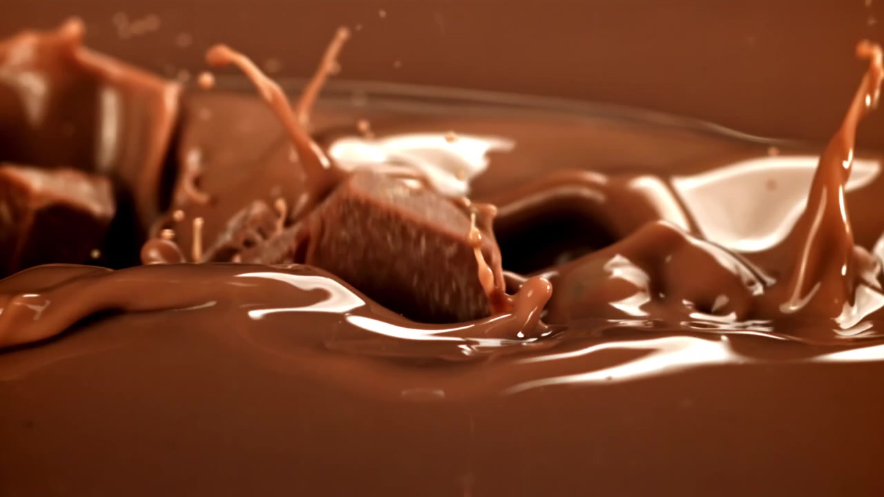 Câmera lenta de pedaços de chocolate salpicando e derramando em chocolate derretido
