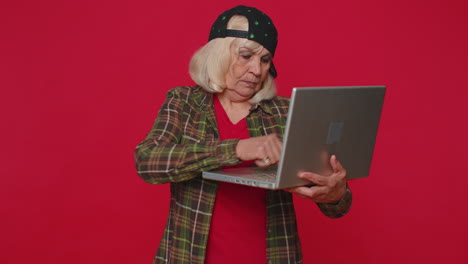 mujer mayor feliz escribiendo en una computadora portátil, trabajando en un proyecto, disfrutando de los resultados, ganando la lotería