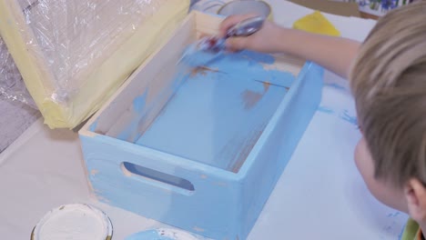 boy paints a box with blue paint. handmade