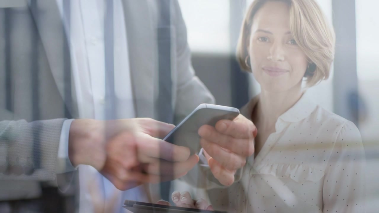Man tapping phone, passing to woman holding tablet, showing biz chart overlay for review