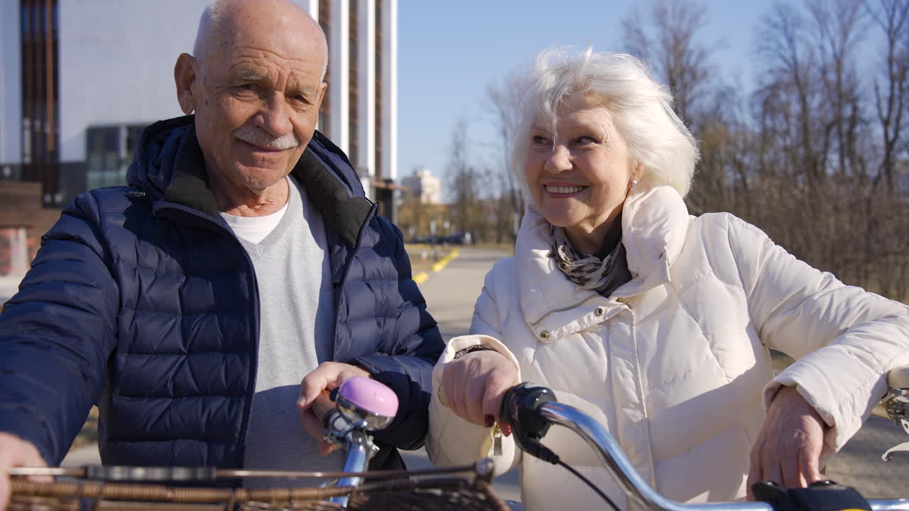 겨울날 공원에서 카메라를 보고 웃고 있는 동안 자전거를 들고 있는 노부부