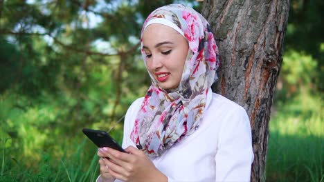 young woman with hijab using smartphone in park