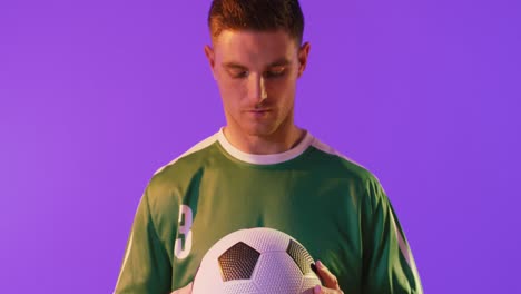 portrait of caucasian male soccer player with football over neon pink lighting