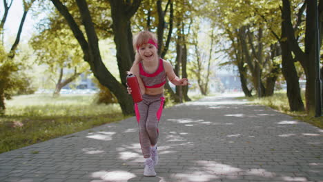 Sport-runner-jogger-child-girl-listen-bluetooth-music-speaker-dancing-to-camera-having-fun-in-park