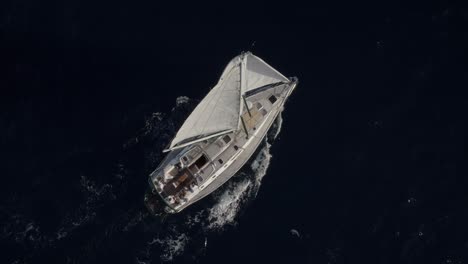 top down to 70 - 80 degree tilted slow tracking shot of monohull sail boat moving around while sailing in dark blue seas