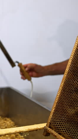 unrecognized man takes the frame and electric knife. apiculturist cleans off the wax from wooden frame. close up. vertical video