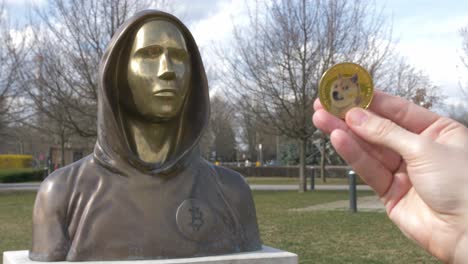 ficha dogecoin junto a la estatua de satoshi nakamoto