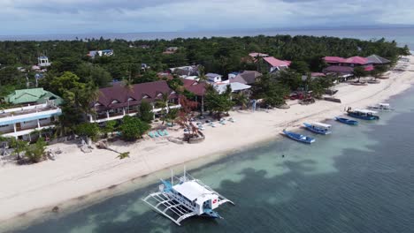 Outrigger-diving-boat-moored-at-beachfront-dive-resorts-on-Malapascua-Island-,-Philippines