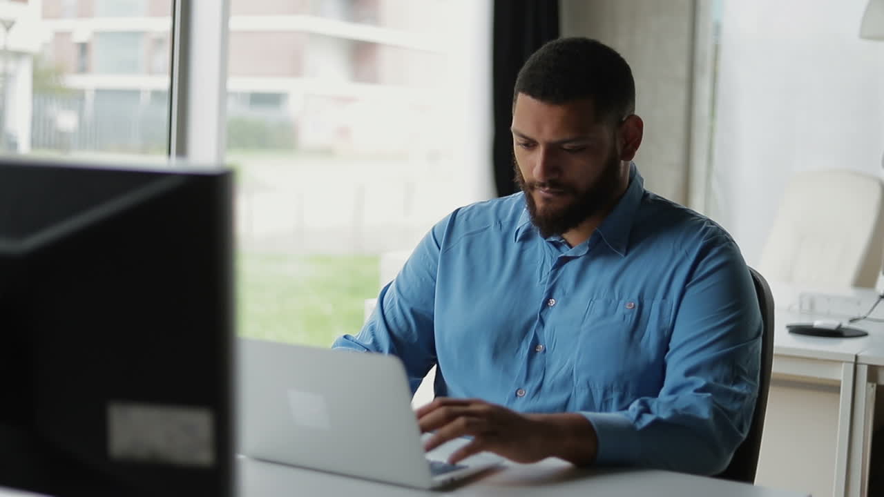 joven hombre de negocios reflexivo escribiendo en una computadora portátil en una oficina moderna.