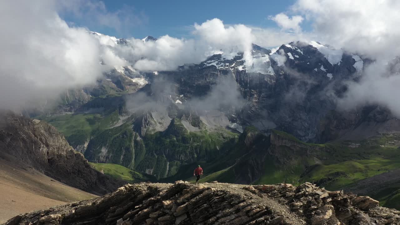 toma aérea de un hombre joven y atlético corriendo la última parte de la cresta hasta la cima del acantilado, deteniéndose y mirando el paisaje grandioso y épico frente a él
