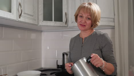 baker monitors temperature of liquid substance in metal container while smiling and swaying gently to rhythm of music in cozy kitchen with overhead cabinets, expressing joy during creative process