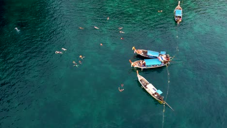 tourists swimming from long tail boats near tropical island