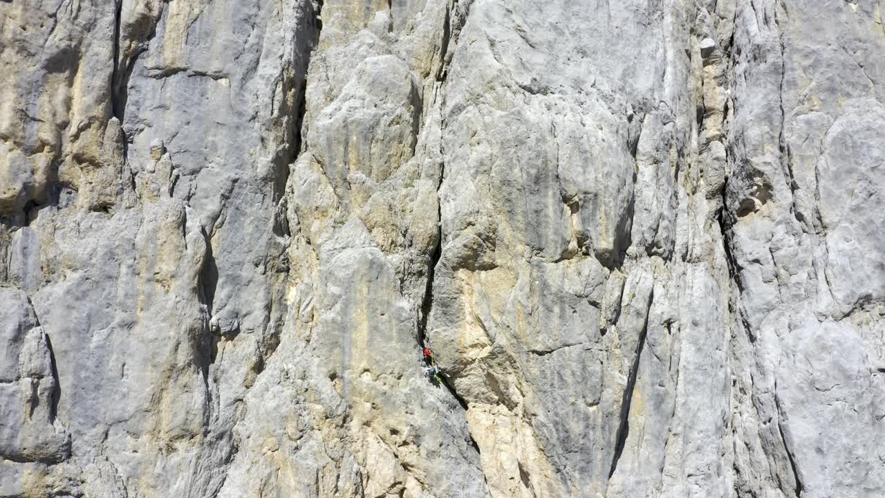 toma aérea hacia atrás de montañero escalando en la pared de un acantilado escarpado durante el día soleado - marmolada, dolomitas