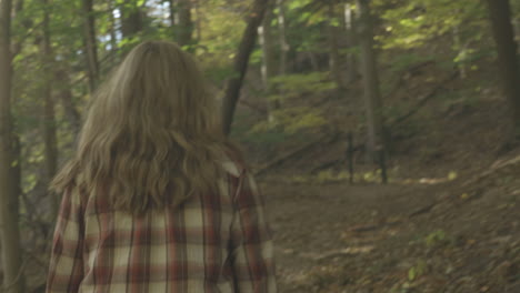 Handheld-over-the-shoulder-shot-following-young-woman-walking-on-a-trail-in-the-woods