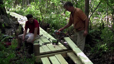 a father and son work on a wooden walkway through the everglades