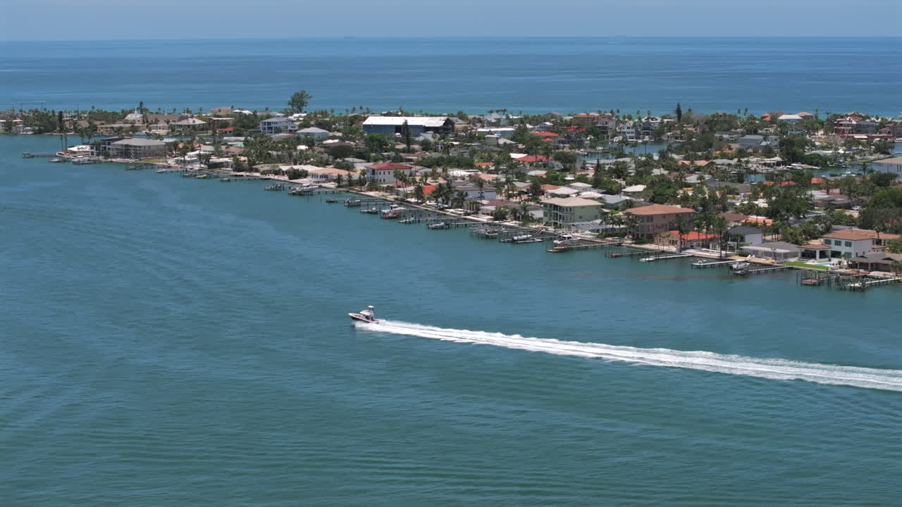 Drone shot of speeding boat on the intracoastal channel of St Pete Beach in Florida with waterfront homes on blue water, capturing serene coastal living, marina lifestyle, and scenic paradise