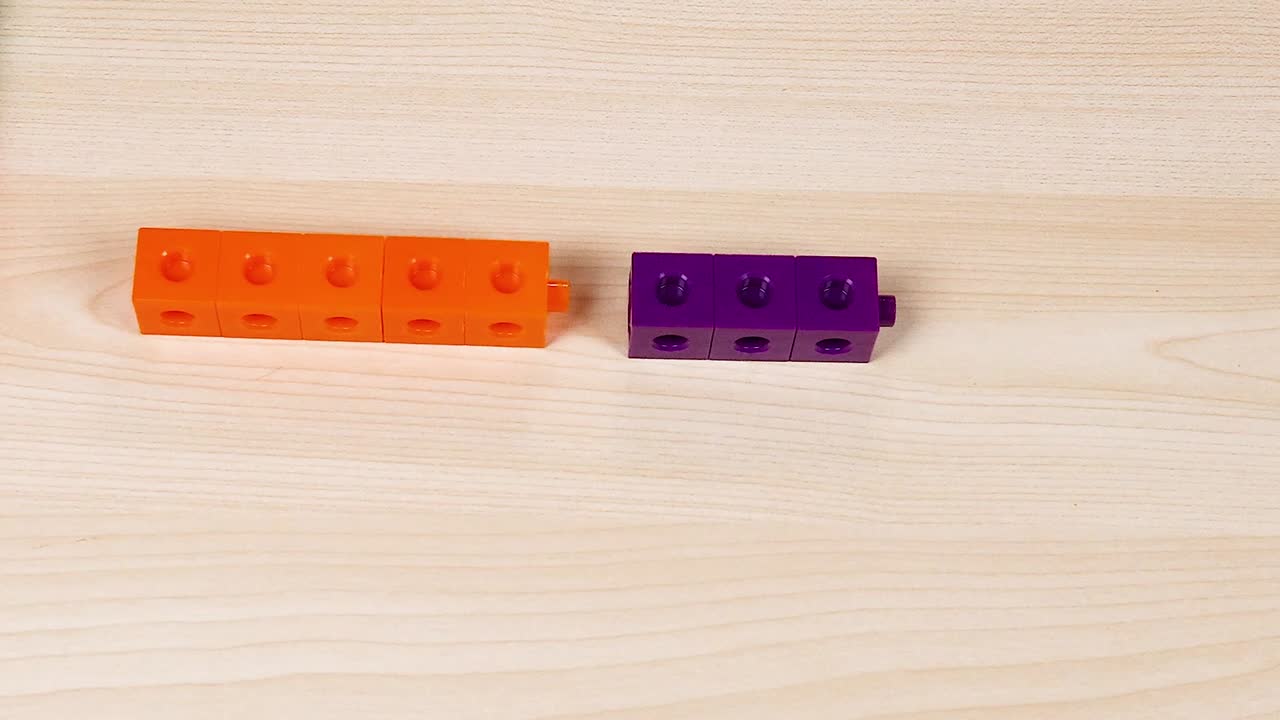 Delle mani assemblano con cura dei blocchi di plastica viola e arancioni su una superficie di legno chiaro.