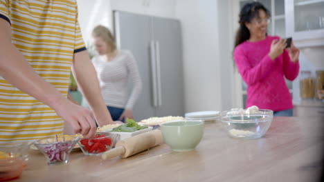 un grupo feliz y diverso de amigos adolescentes usando teléfonos inteligentes y haciendo pizza en la cocina, en cámara lenta