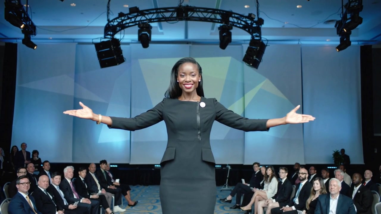 Mujer afroamericana entrando desde el escenario, caminando por la pasarela en un salón con un vestido ajustado, presentando con un pin de solapa