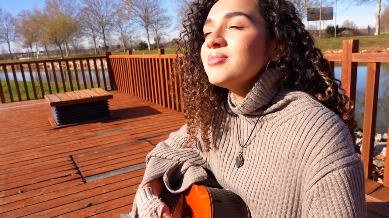 Happy young female musician playing acoustic guitar outdoors on a sunny day