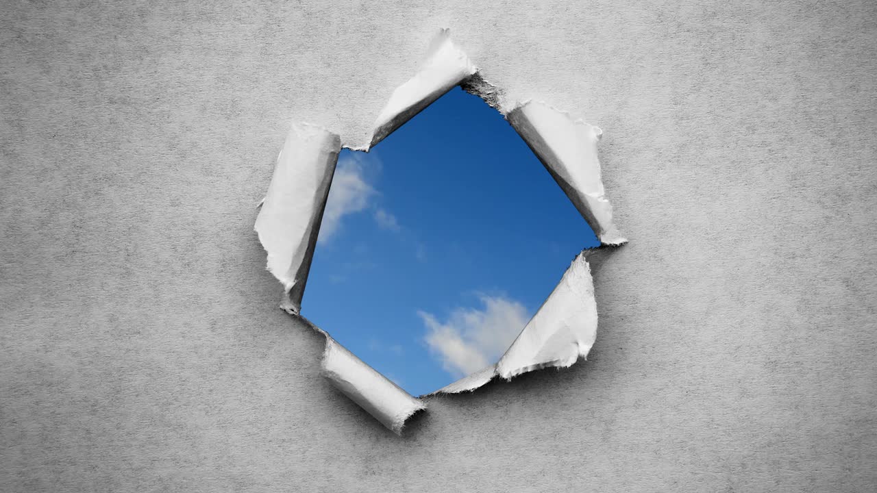 Creative 4k time laps video of fast moving clouds in the blue sky that are visible through a circle hole with torn edges in old retro grunge vintage paper.