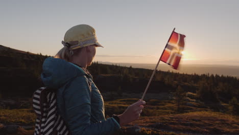 ein reisender mit der flagge norwegens in der hand trifft den sonnenaufgang auf dem gipfel des berges und genießt t