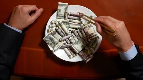 hands of a businessman with chopsticks and dollar rolls. eating dollars. 4k.