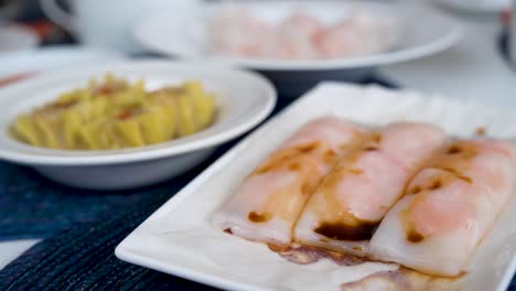 a steamed shrimp rice noodle roll dish is seen in the foreground displayed on a table as part of a cantonese culinary food and dim sum experience