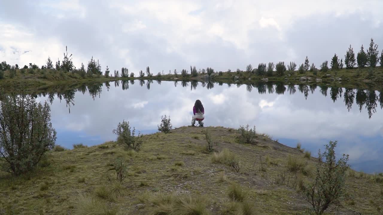 A Woman Seated Near Lakeshore With Mirror Reflection In Huaraz, Peru. Static Shot