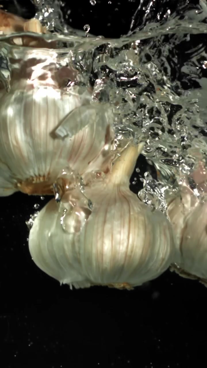 Teste d'aglio fresche che schizzano in acqua limpida al rallentatore