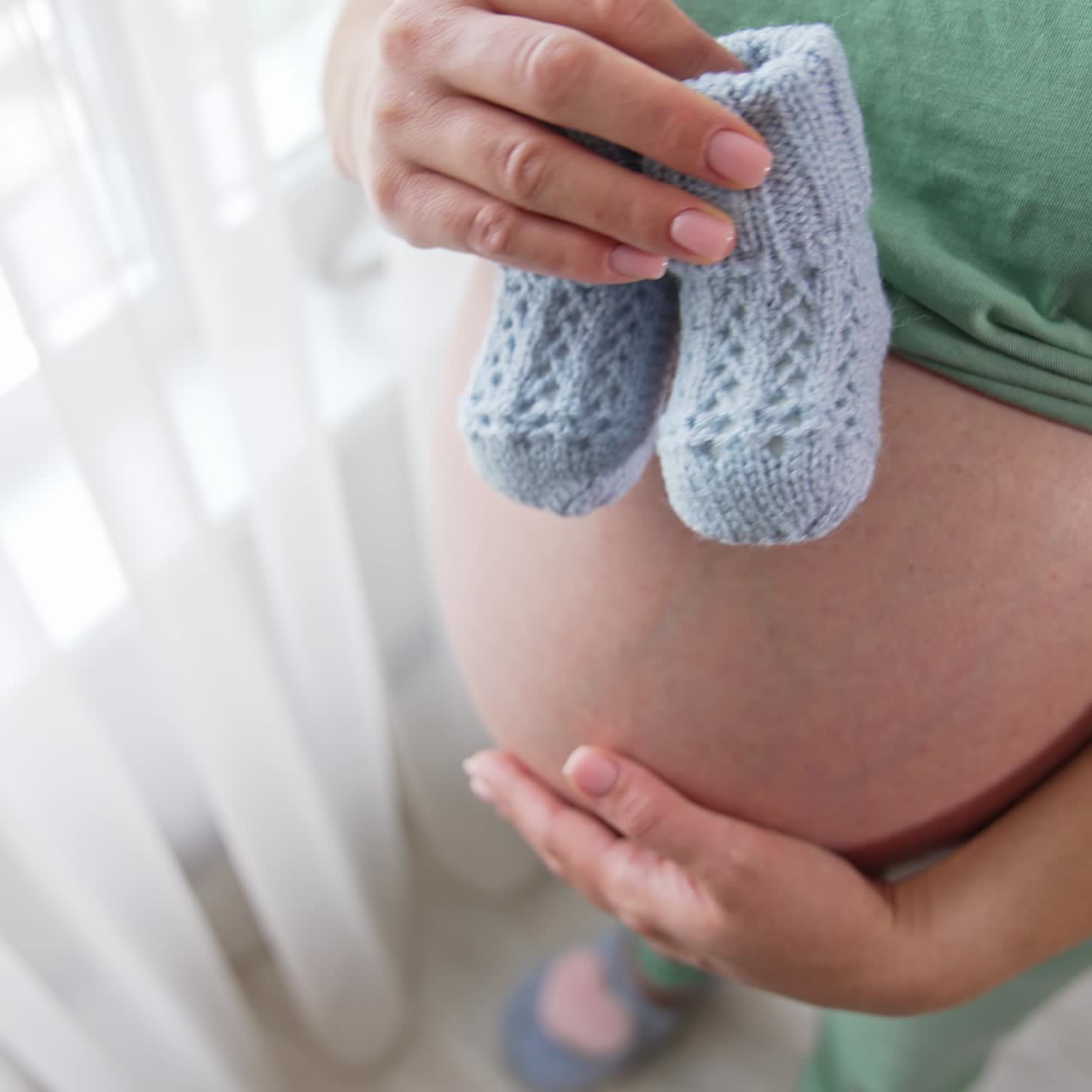 Donna incinta che tiene due graziose scarpine da neonato sopra la pancia. Mette le scarpine sulla pancia e le muove lentamente sulla pancia. Vista dall'alto
