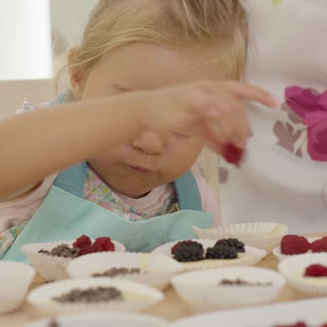 serious child placing berries on muffins