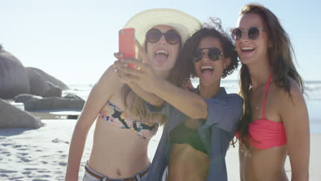 group of girl friends taking selfies on the beach using pink phone