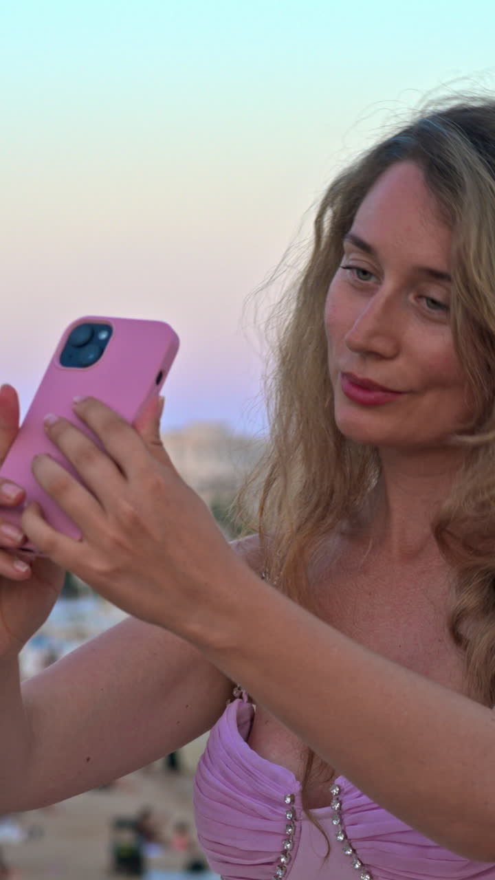 Donna con vestito rosa che scatta foto sulla spiaggia di sera a Cannes, in Francia. Verticale