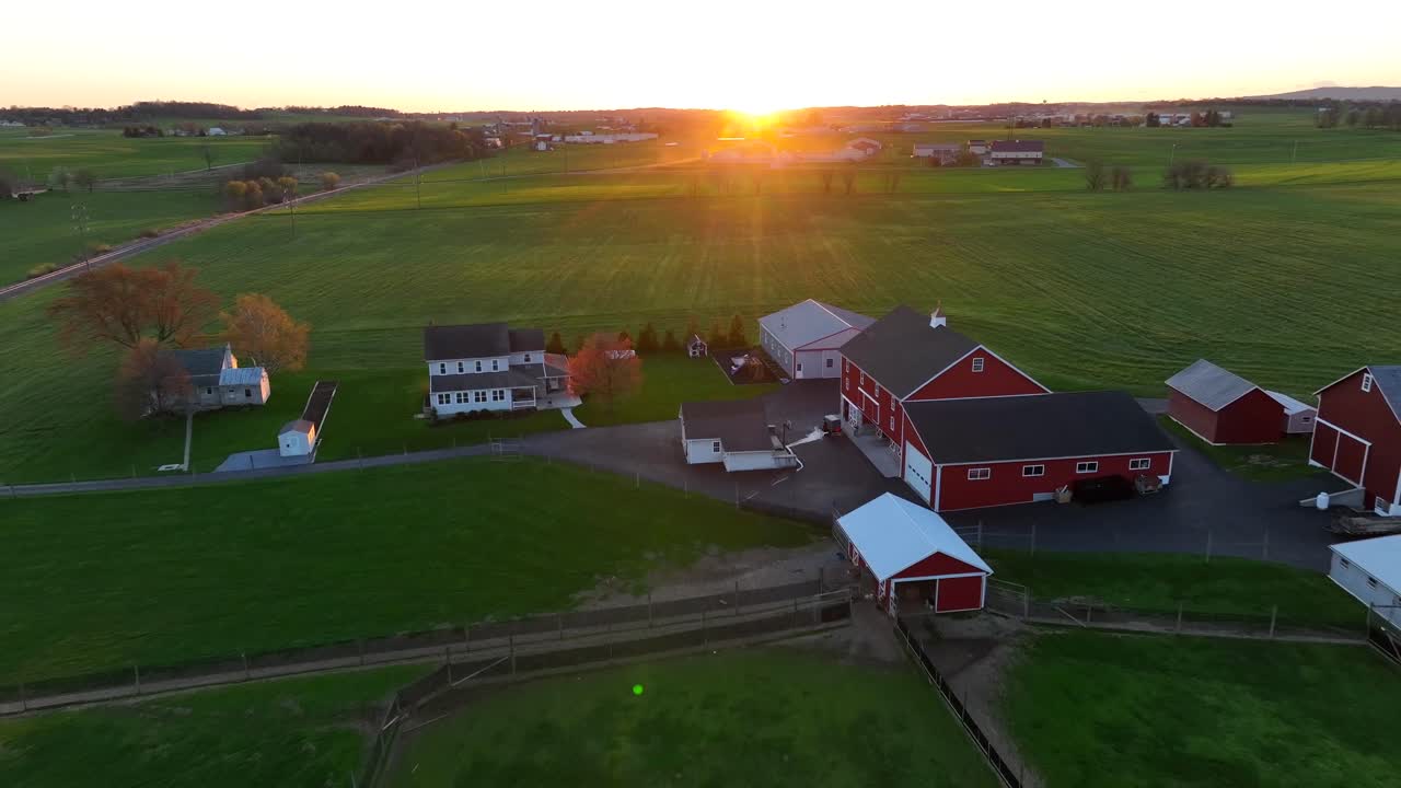 Gylden solnedgang over grønne marker og bondehuse med røde lader på landet i USA.