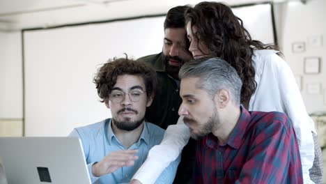 compañeros de trabajo sonrientes hablando, haciendo gestos y mirando la computadora portátil en la oficina