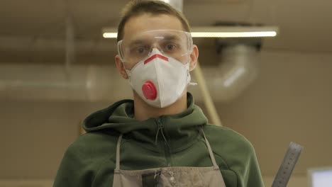 portrait of worker carpenter with respirator and glasses in workshop, holds the ruler